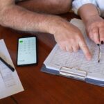 Paar sitzt mit Unterlagen und Taschenrechner am Küchentisch und rechnet eine Finanzierung durch