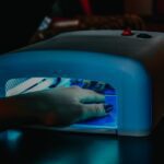 maniko nails - A hand with manicured nails being cured under a blue LED lamp for gel polish.